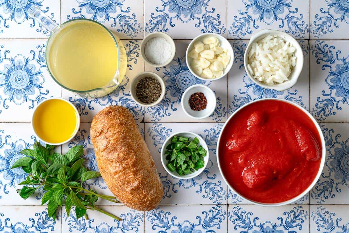 Ingredients for pappa al pomodoro including whole san marzano tomatoes, ciabatta bread, olive oil, red pepper flakes, garlic, onion, basil, vegetable broth, salt and pepper.