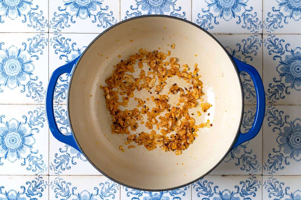 Chopped onion, sliced garlic and red pepper flakes being sauteed in a large pot.