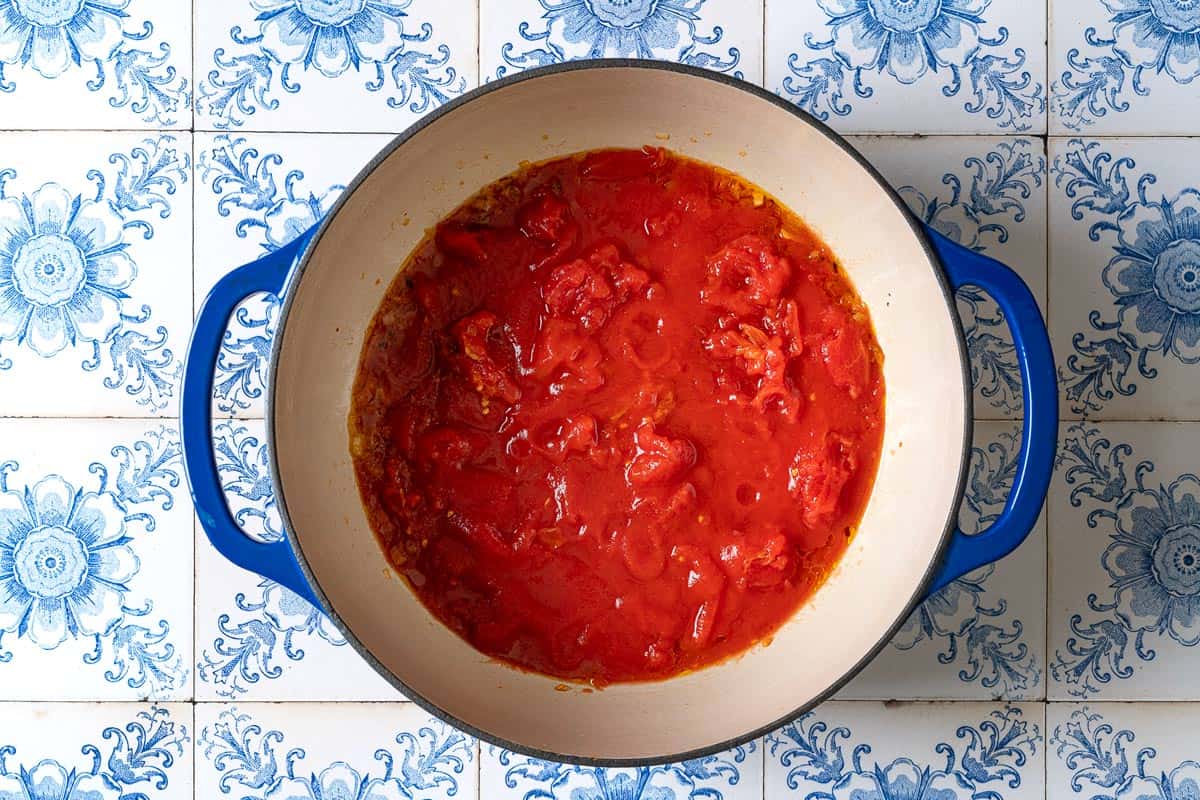 An overhead photo of a large pot with the sauteed garlic, onions and the whole san marzano tomatoes.