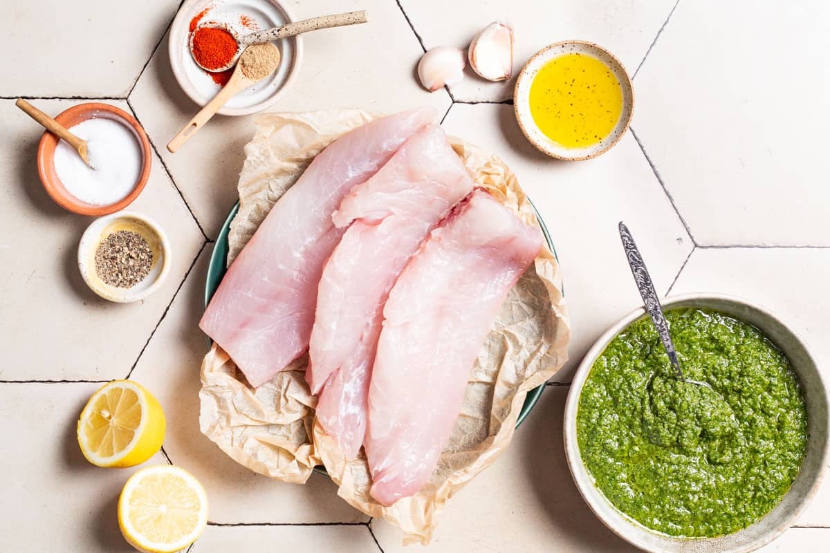 ingredients for baked red snapper including red snapper fillets, lemons, garlic, olive oil, paprika, coriander, salt, pepper and zhoug.