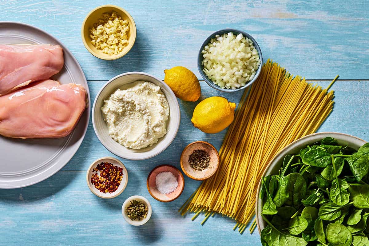 Ingredients for lemon chicken pasta including spaghetti, ricotta, lemon, salt, pepper, red pepper flakes, onion, garlic, chicken breast, oregano, and baby spinach.