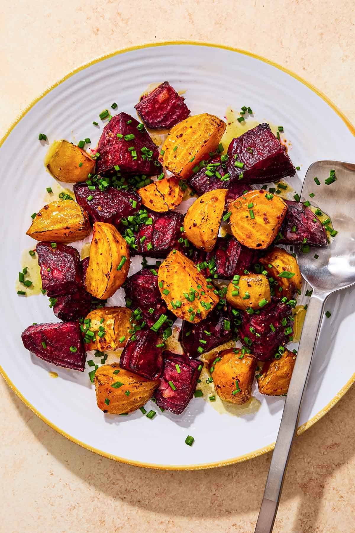 An overhead photo of roasted beets on a platter, topped with chives and a drizzle of apple cider vinaigrette with a serving spoon.
