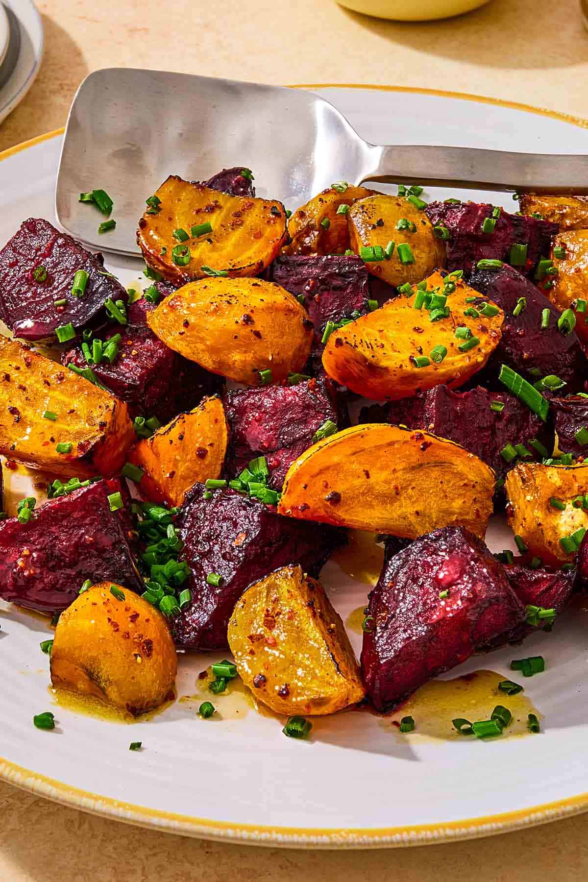 A close up of roasted beets on a platter, topped with chives and a drizzle of apple cider vinaigrette with a serving spoon.