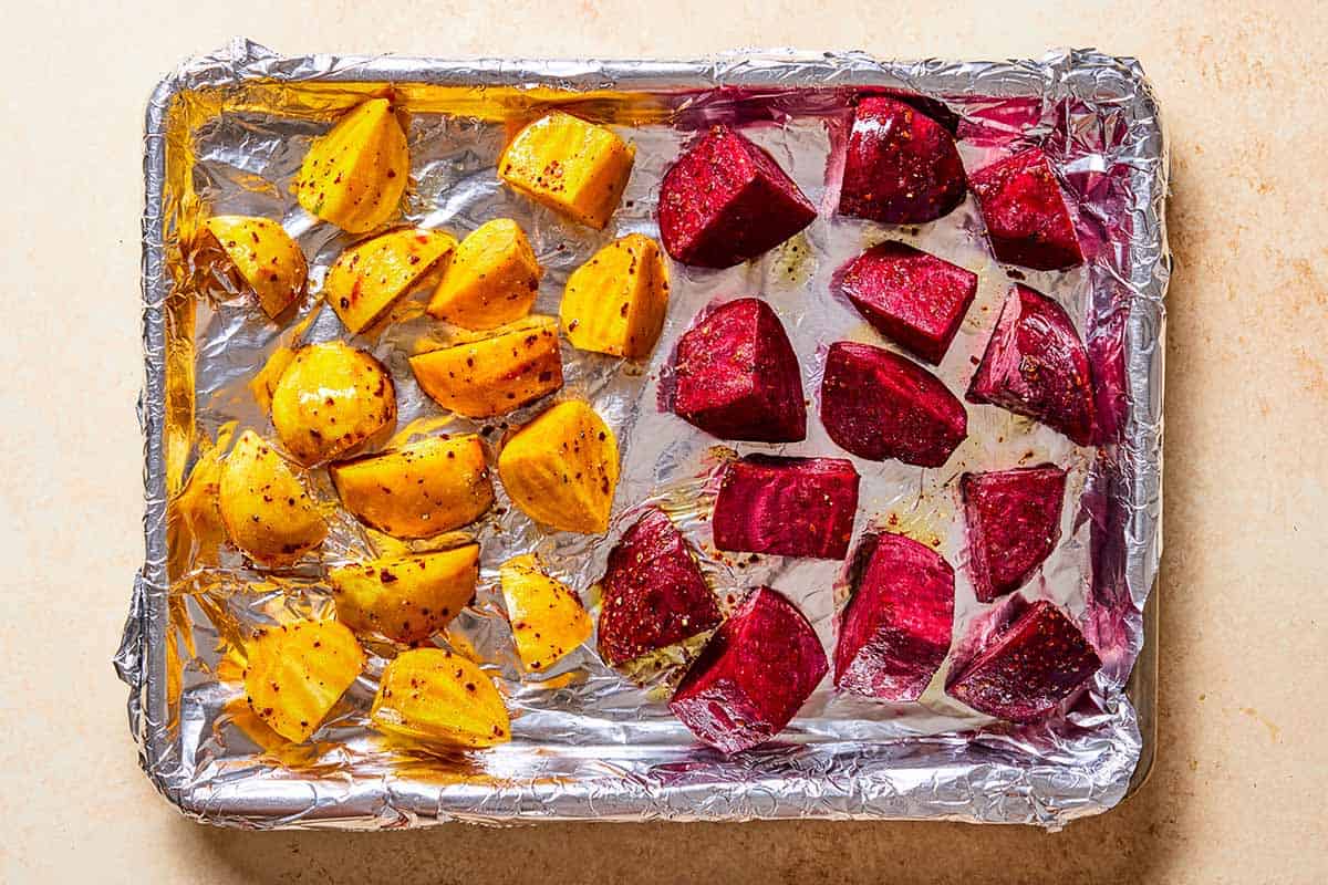 Uncooked cubes of golden beets and red beets spread on a foil lined baking sheet.