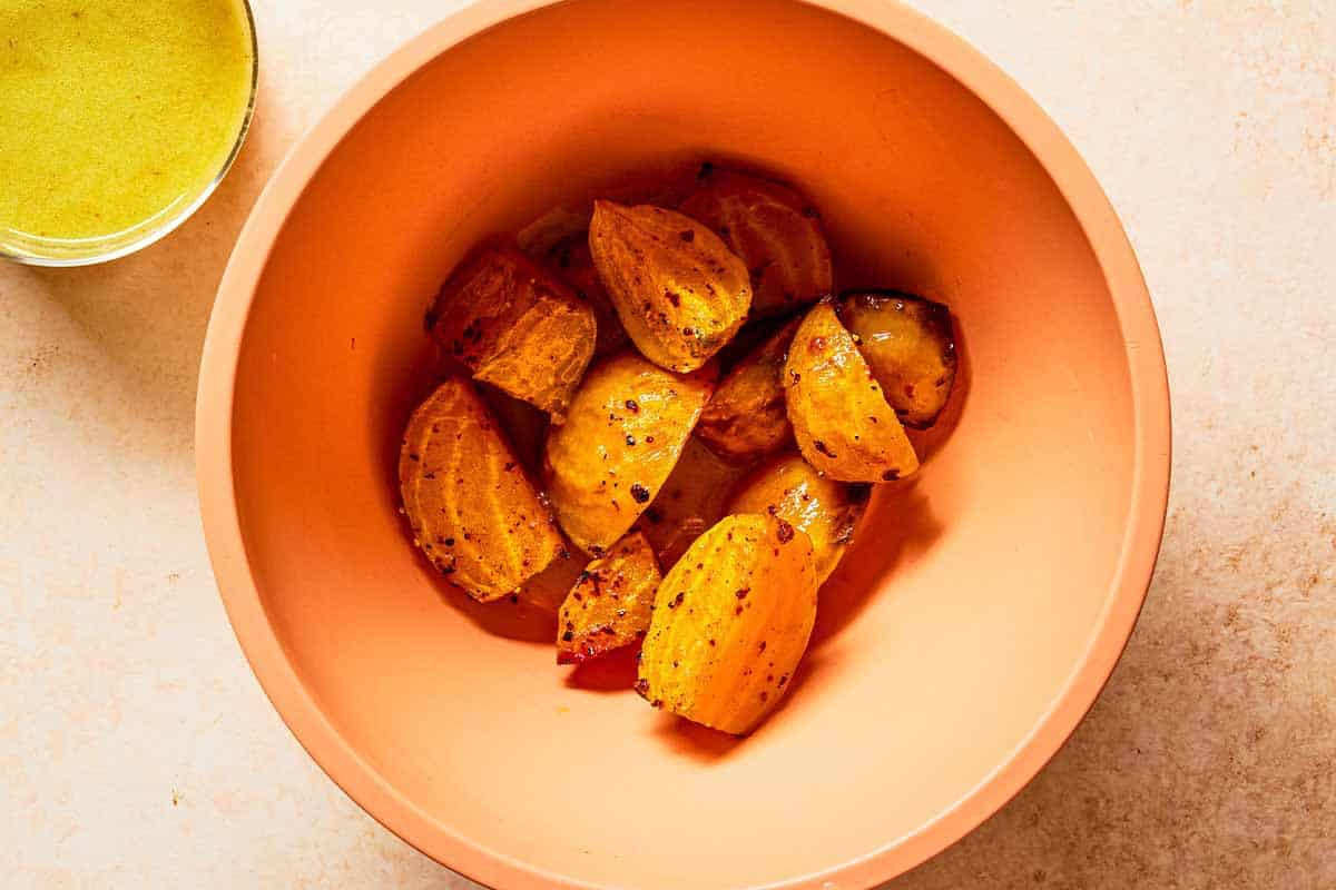 Roasted golden beets tossed in apple cider vinaigrette in a mixing bowl. Next to this is a small bowl of the vinaigrette.