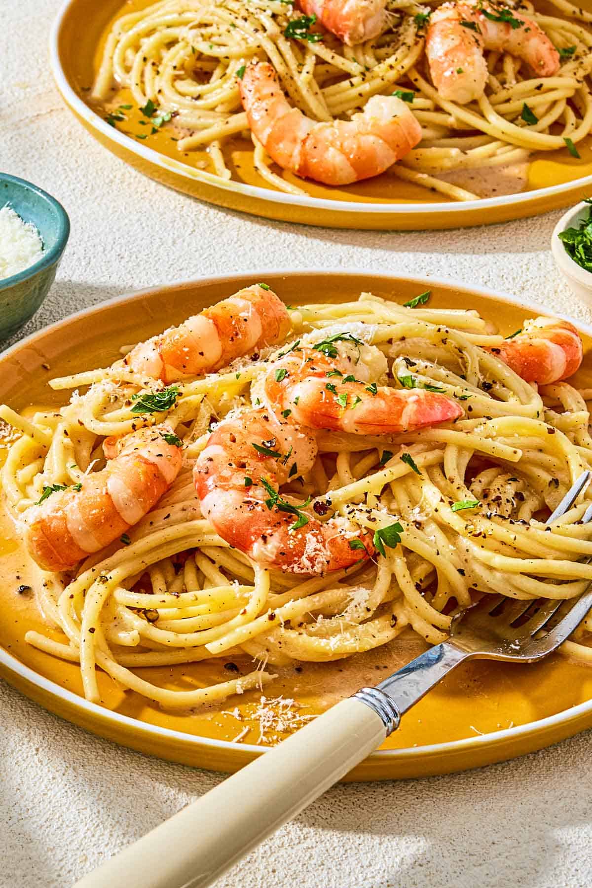 A close up of a serving of shrimp cacio e pepe on a plate with a fork with another in the background.