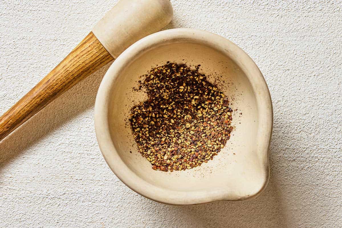 Ground peppercorns in a bowl with a pestle next to it.