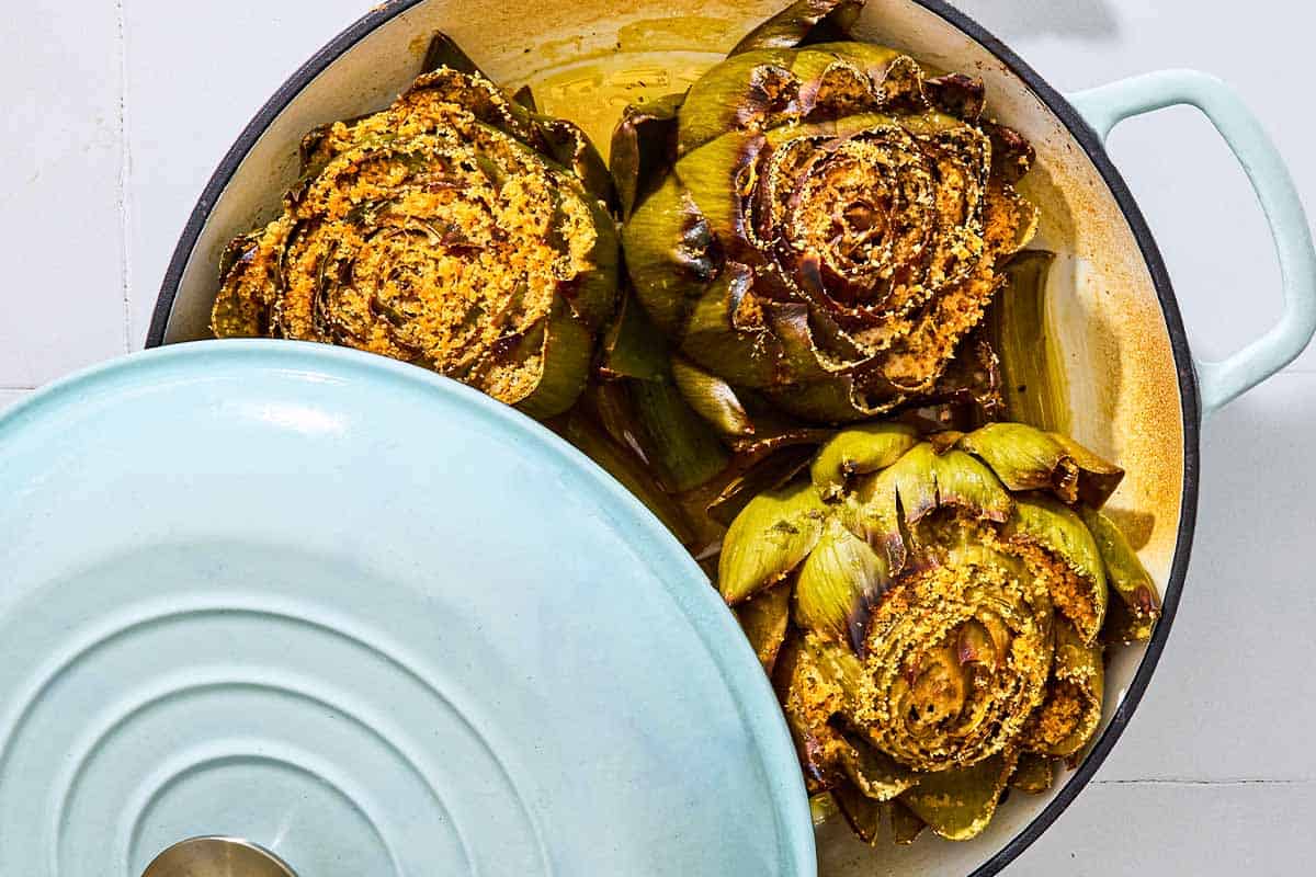 An overhead photo of 3 cooked stuffed artichokes in a pot with a lid.