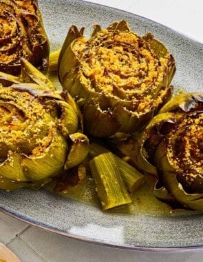 Four cooked stuffed artichokes on a serving patter with their stems.