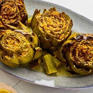 Four cooked stuffed artichokes on a serving patter with their stems.