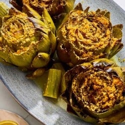 An overhead photo of four cooked stuffed artichokes on a serving patter with their stems. Next to this is a plate of lemon wedges.