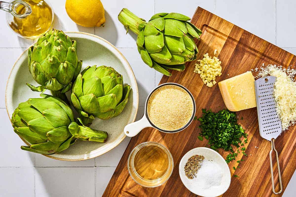 Ingredients for stuffed artichokes including globe artichokes, white wine, breadcrumbs, garlic, parsley, pecorino romano cheese, salt, pepper, olive oil and lemon.