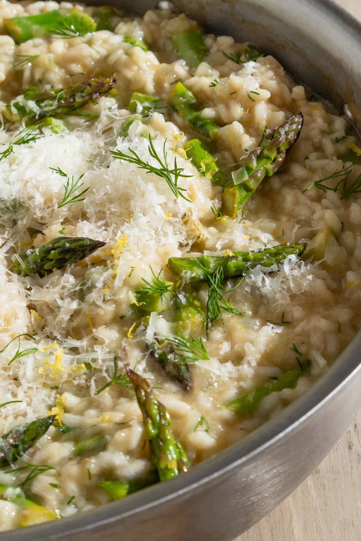 A close up of asparagus risotto topped with parmesan and dill in a skillet.