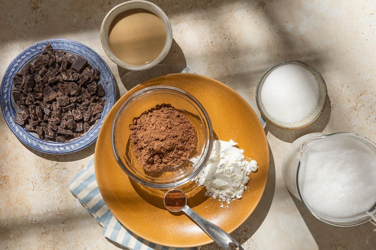 Ingredients for tahini chocolate pudding including cocoa powder, sugar, cornstarch, baharat spice blend, salt, almond milk, chocolate and tahini.