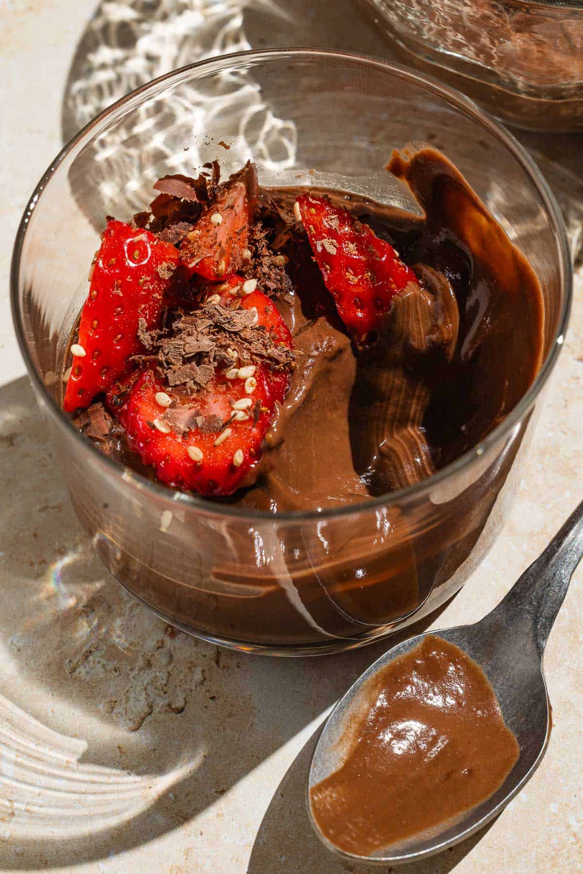 A close up of a bowl of vegan chocolate pudding garnished with sliced fresh strawberries with a spoon next to it.