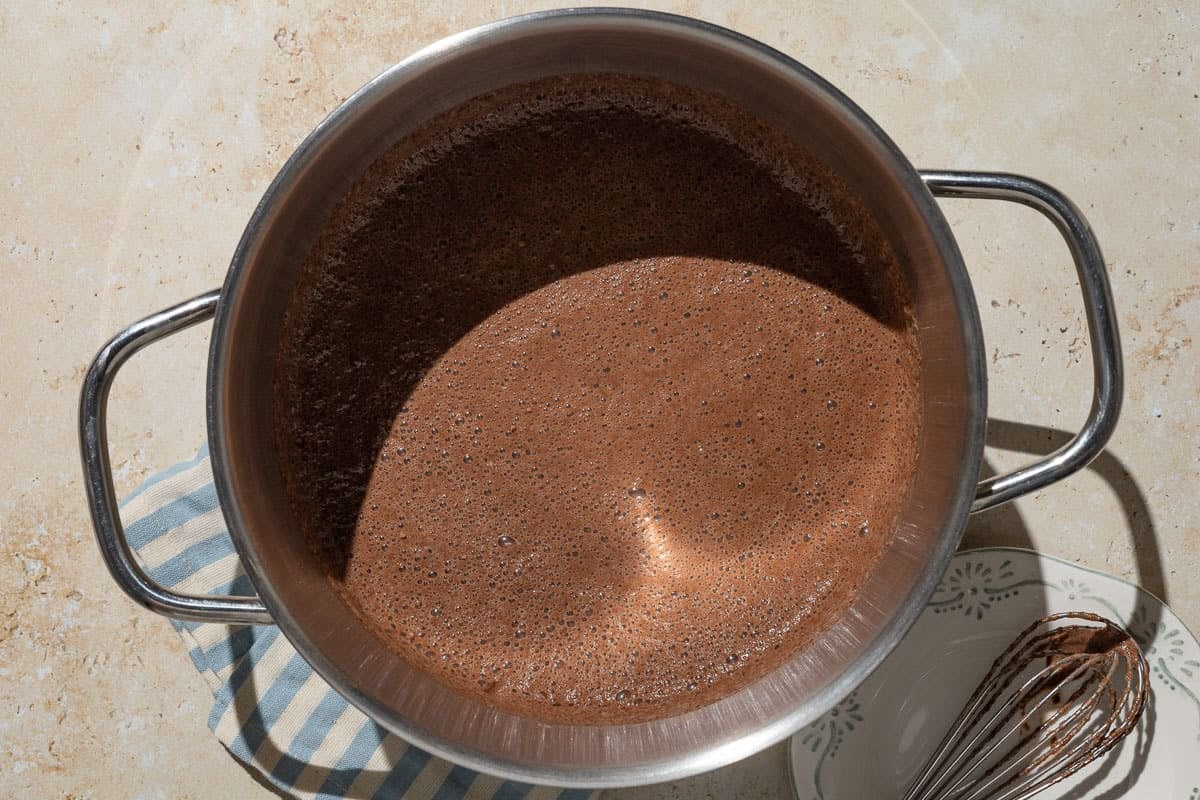 An overhead photo of pudding beginning to cook in a pot. Next to this is a whisk on a plate.