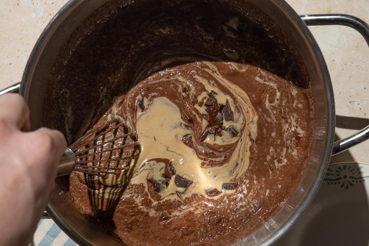 An overhead photo of the the chopped chocolate and tahini being stirred into vegan chocolate pudding with a whisk.