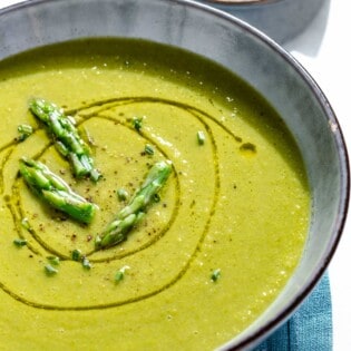 A close up of a bowl of asparagus soup. Next to this is a small plate of lemon wedges.