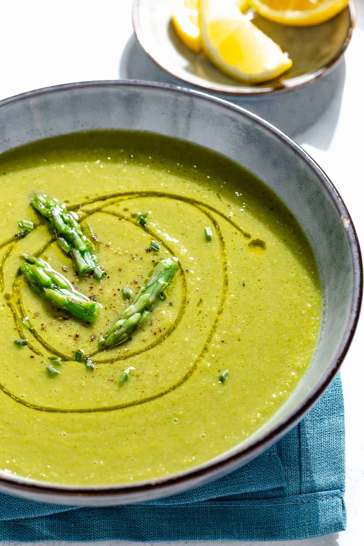 A close up of a bowl of asparagus soup. Next to this is a small plate of lemon wedges.