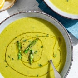 An overhead photo of two bowls of asparagus soup, one with a spoon. Next to these is a small plate of lemon wedges.