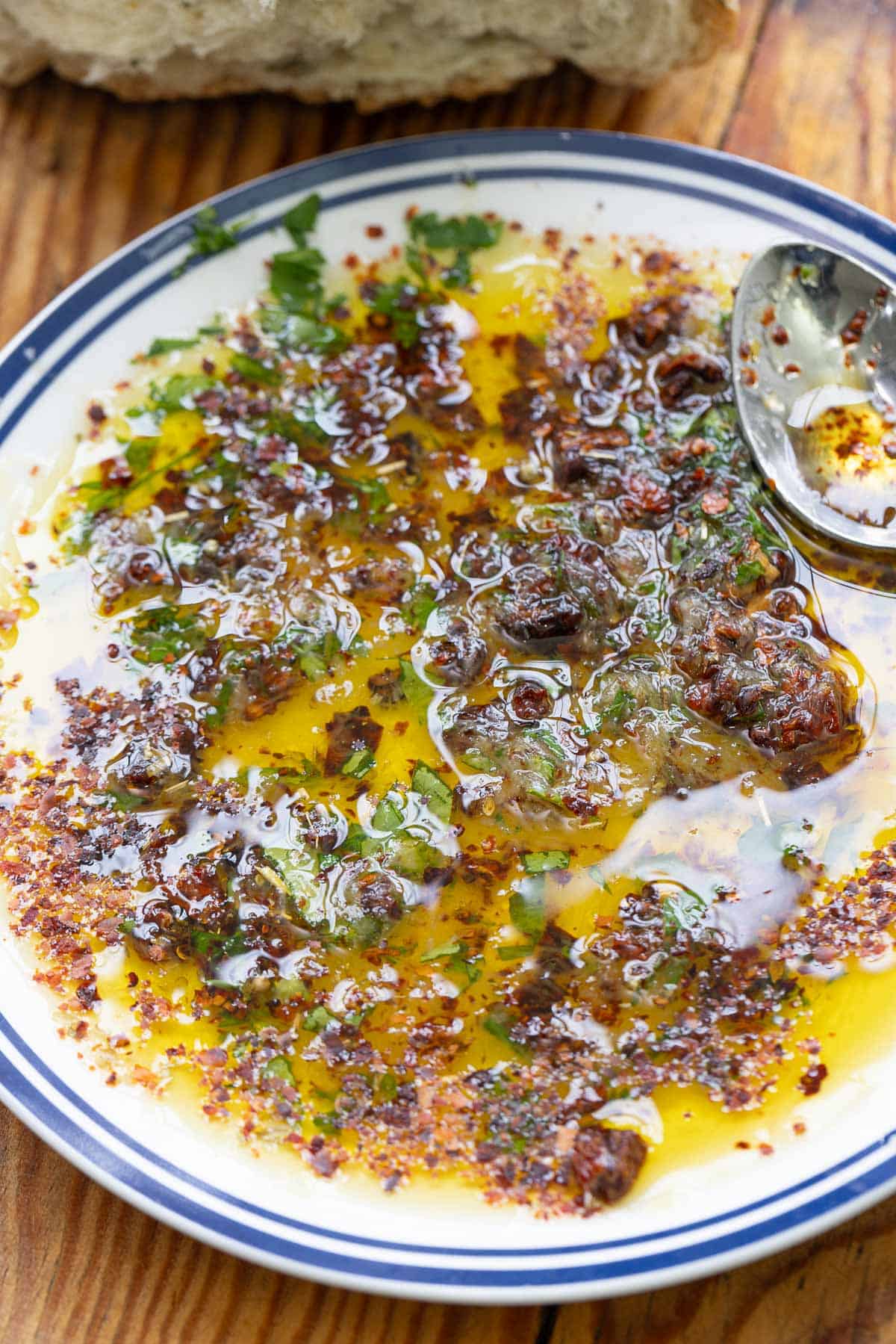 A close up of bread dipping oil on a plate with a spoon.