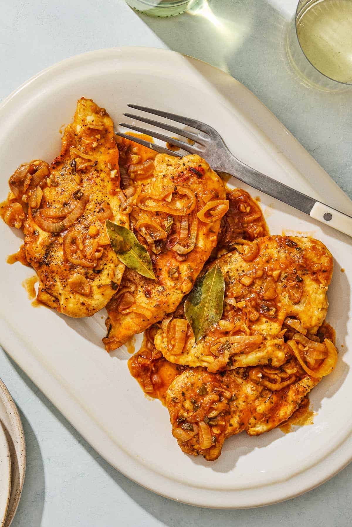 An overhead photo of braised chicken breasts on a serving platter with a serving fork.