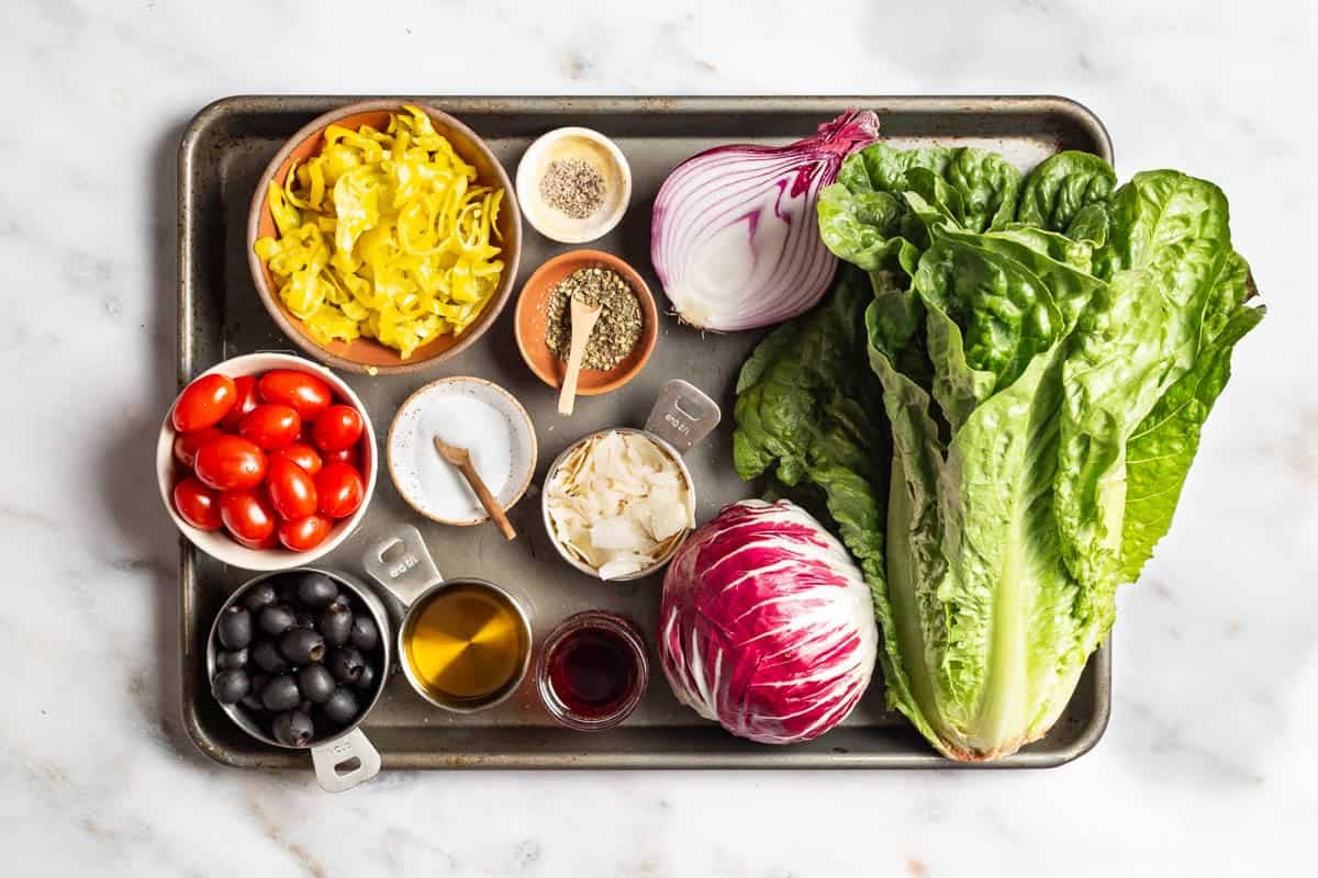 Ingredients for Italian salad including romaine lettuce, radicchio, red onion, cherry tomatoes, black olives pepperoncini, shaved parmesan, salt, pepper, olive oil, red wine vinegar and Italian seasoning.