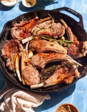 Pan seared lamb chops in a cast iron skillet surrounded by small bowls of salt, pepper and za'atar, and a kitchen towel.