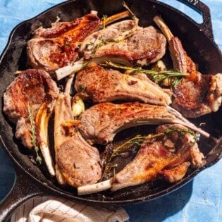Pan seared lamb chops in a cast iron skillet surrounded by small bowls of salt, pepper and za'atar, and a kitchen towel.