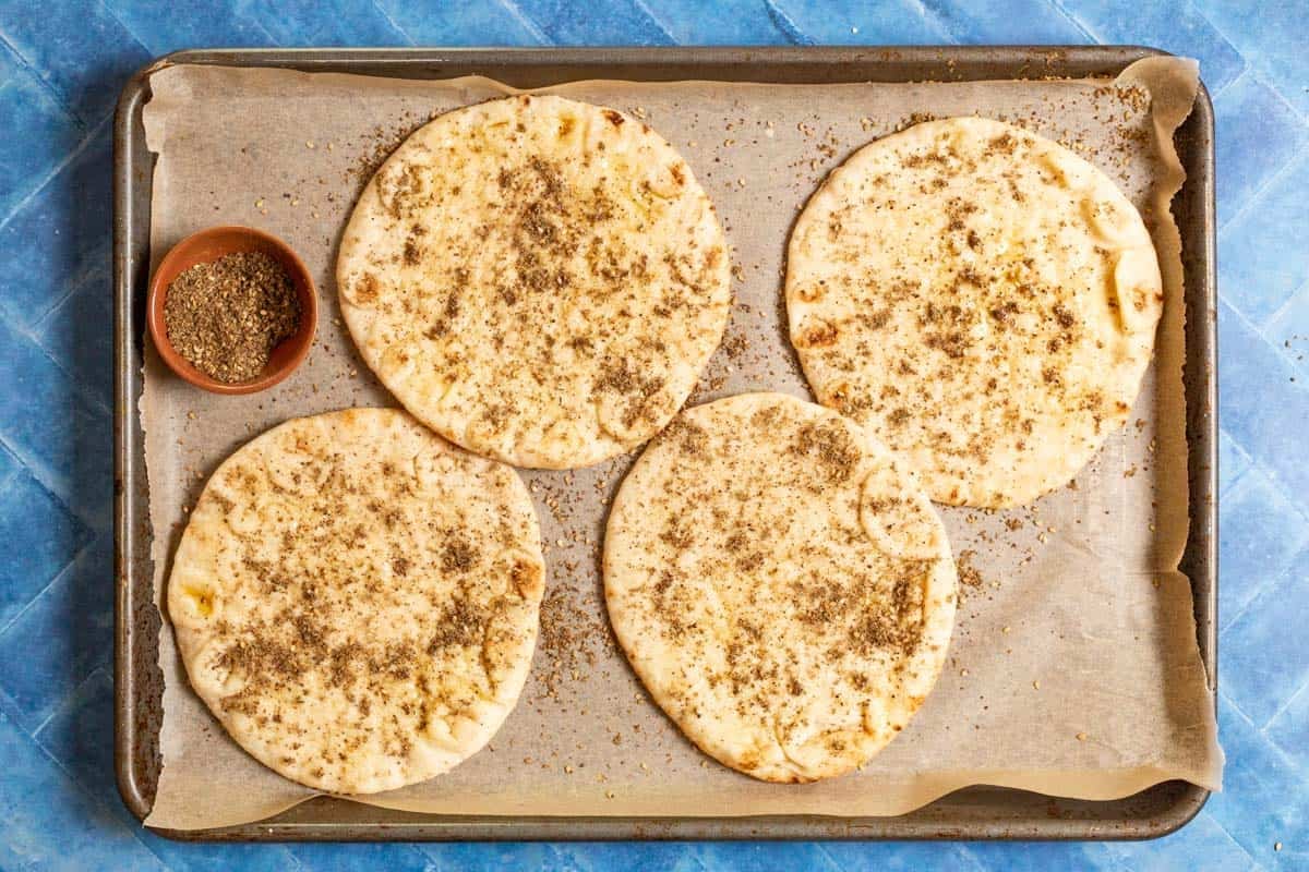 seasoned flatbread on a parchment lined baking sheet with a bowl of za'atar.