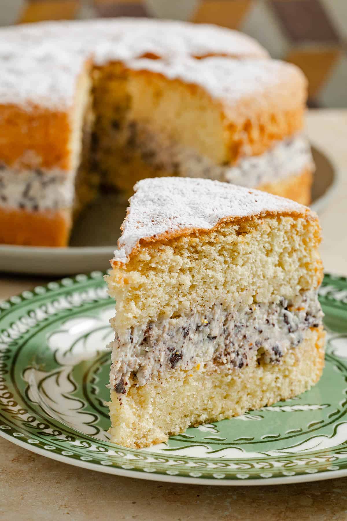 A slice of the easy cassata cake on a plate, with the rest of the cake on a serving platter in the background.