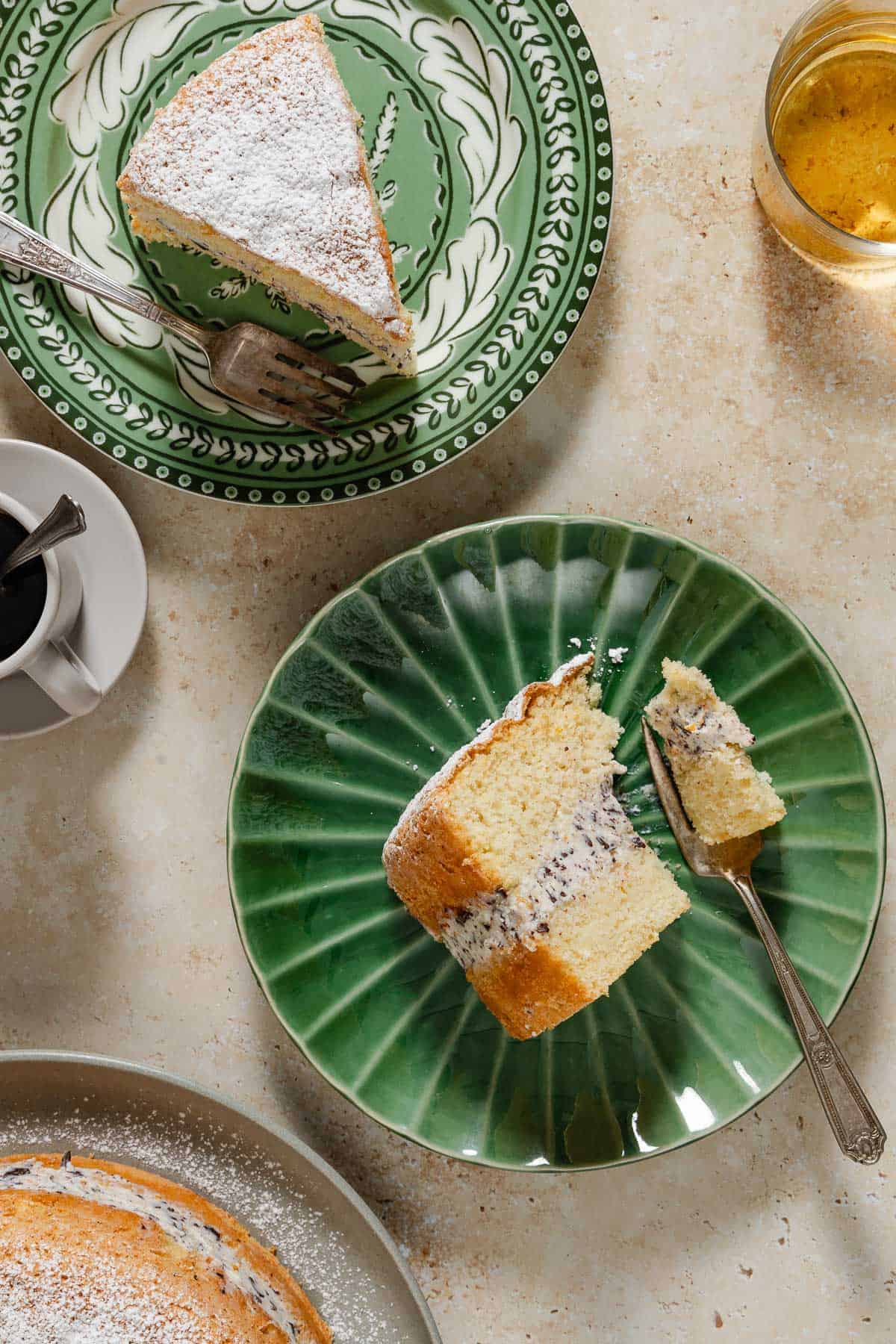 An overhead photo of two slices of easy cassata cake on two plates with forks. Surrounding this is a cup of coffee, a glass of juice, and the rest of the cake on a serving platter.
