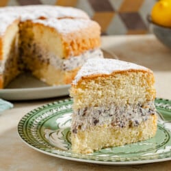 A slice of the easy cassata cake on a plate, with the rest of the cake on a serving platter and a bowl of citrus fruit in the background.