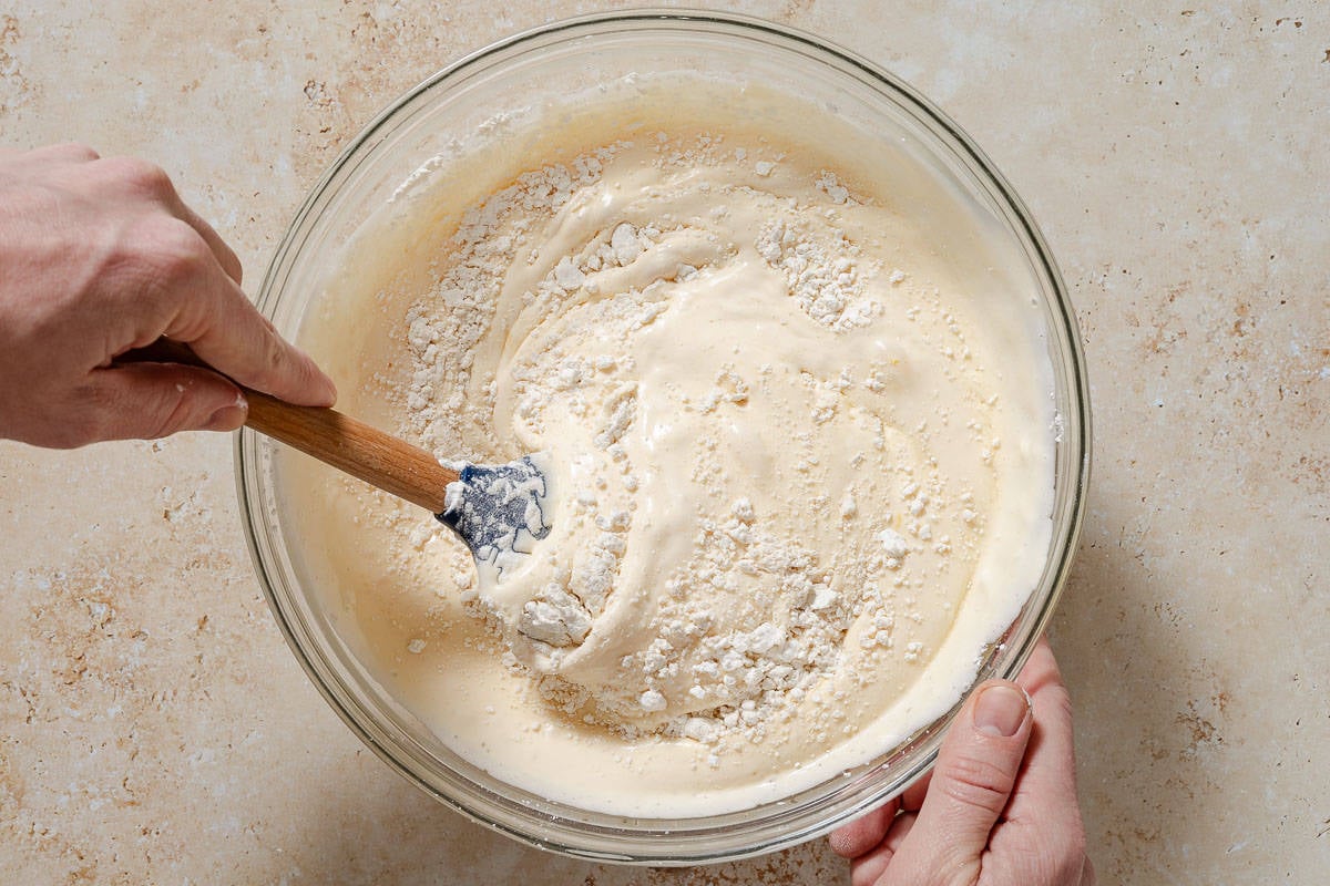 Flour being folded into the egg mixture in a bowl with a spatula.