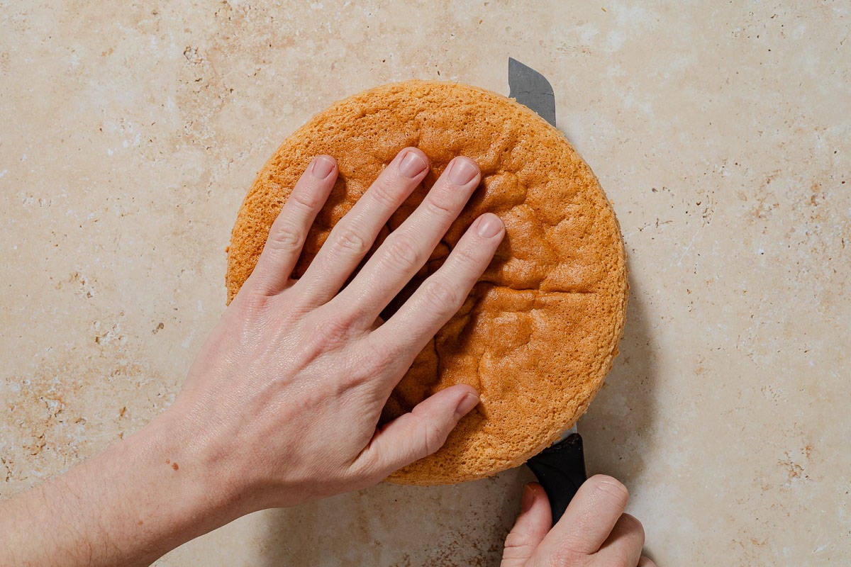 The just baked cassata cake being cut in half horizontally with a knife.