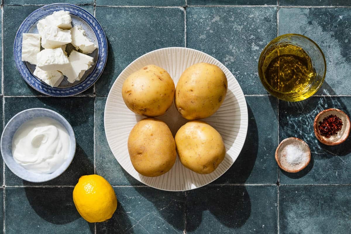 Ingredients for stuffed potatoes with feta including potatoes, feta, salt. olive oil, greek yogurt, aleppo pepper, and lemon