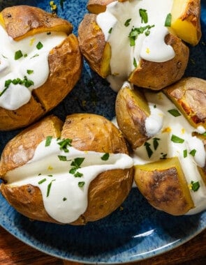 An overhead close up photo of 4 stuffed potatoes with feta on a serving platter sitting on a wooden cutting board.