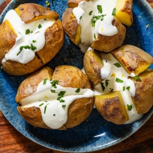 An overhead close up photo of 4 stuffed potatoes with feta on a serving platter sitting on a wooden cutting board.