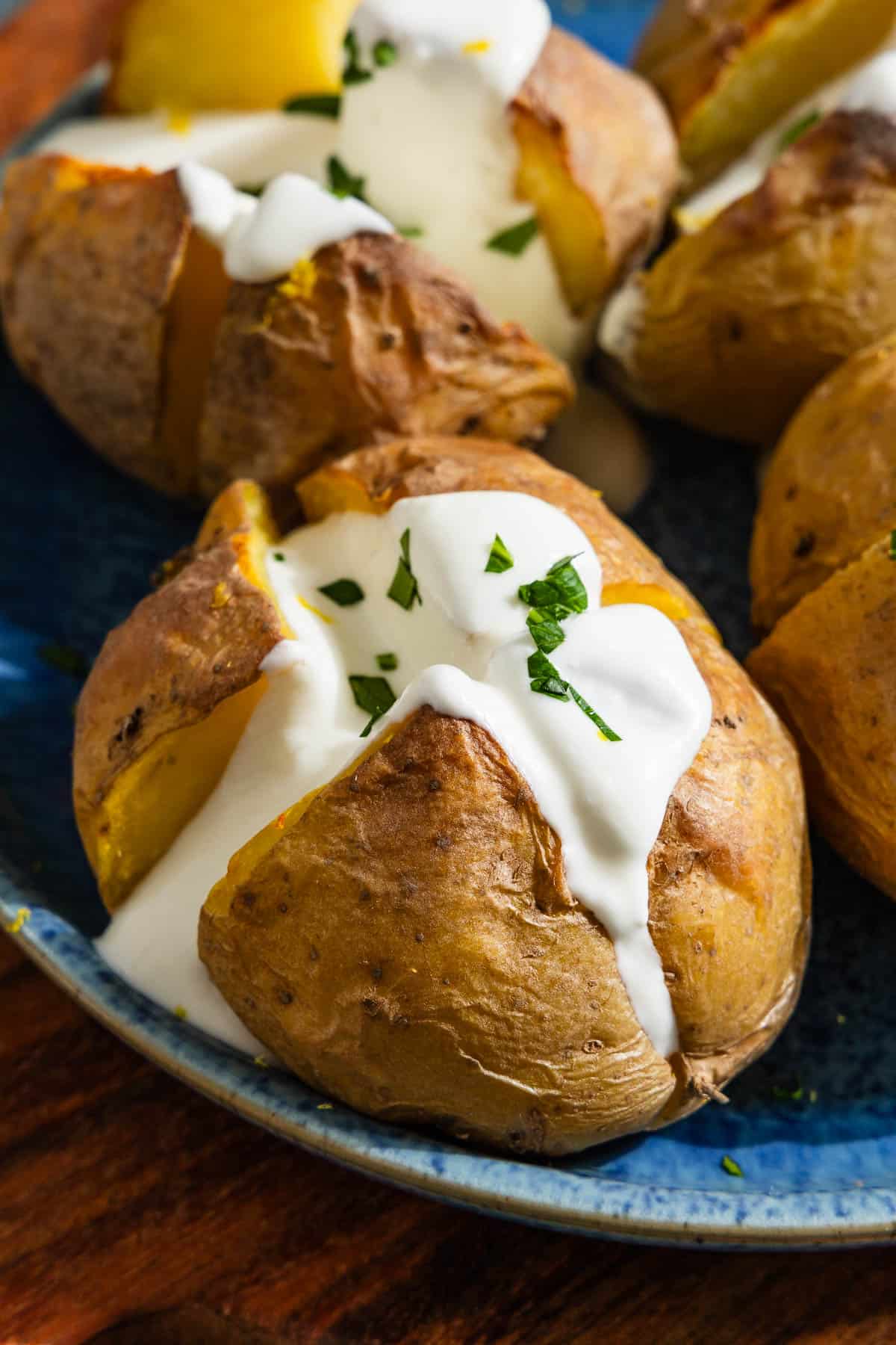 A close up of a stuffed potato with feta on a serving platter with other stuffed potatoes in the background.