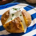 A close up of a stuffed potato with feta on a plate.