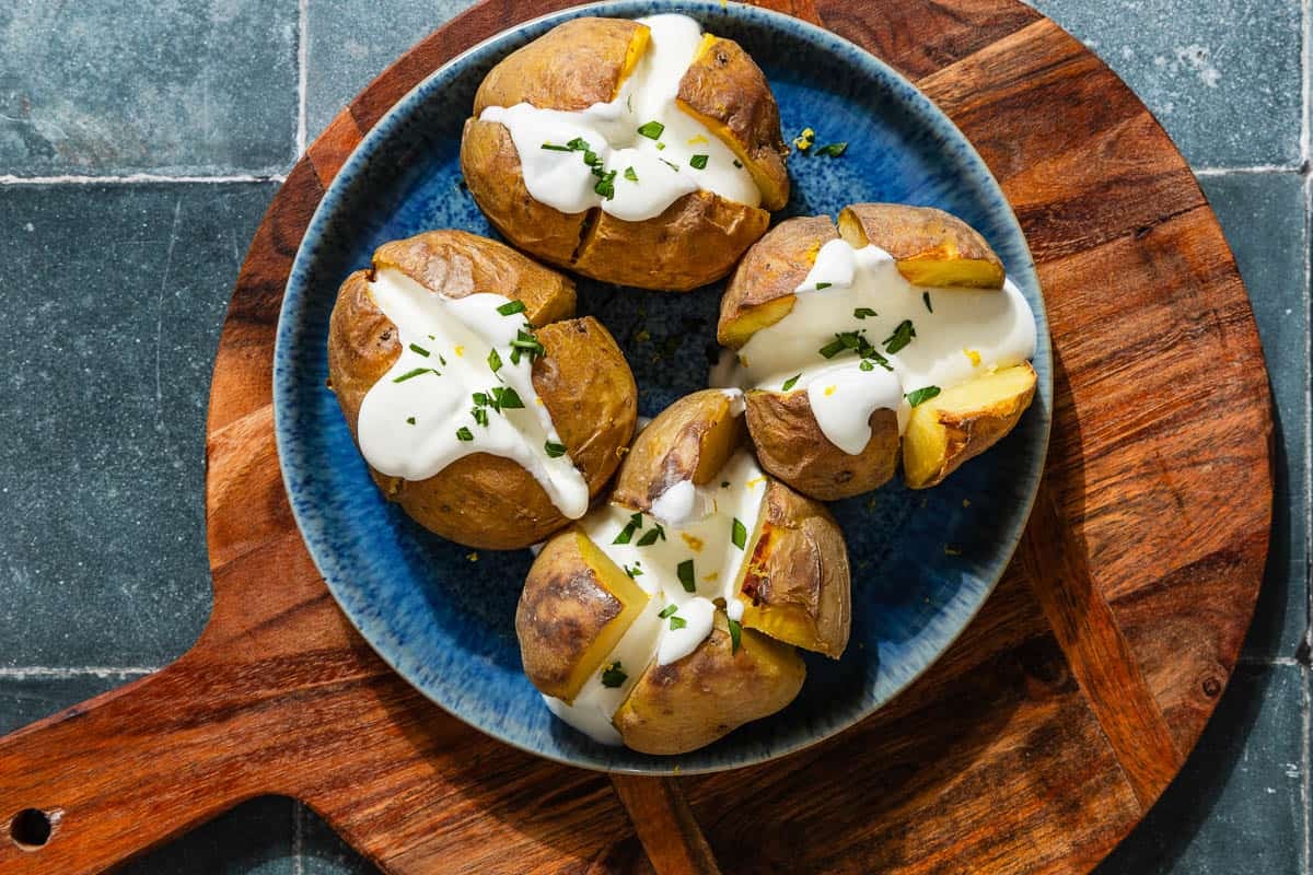 An overhead photo of 4 stuffed potatoes with feta on a serving platter sitting on a wooden cutting board.