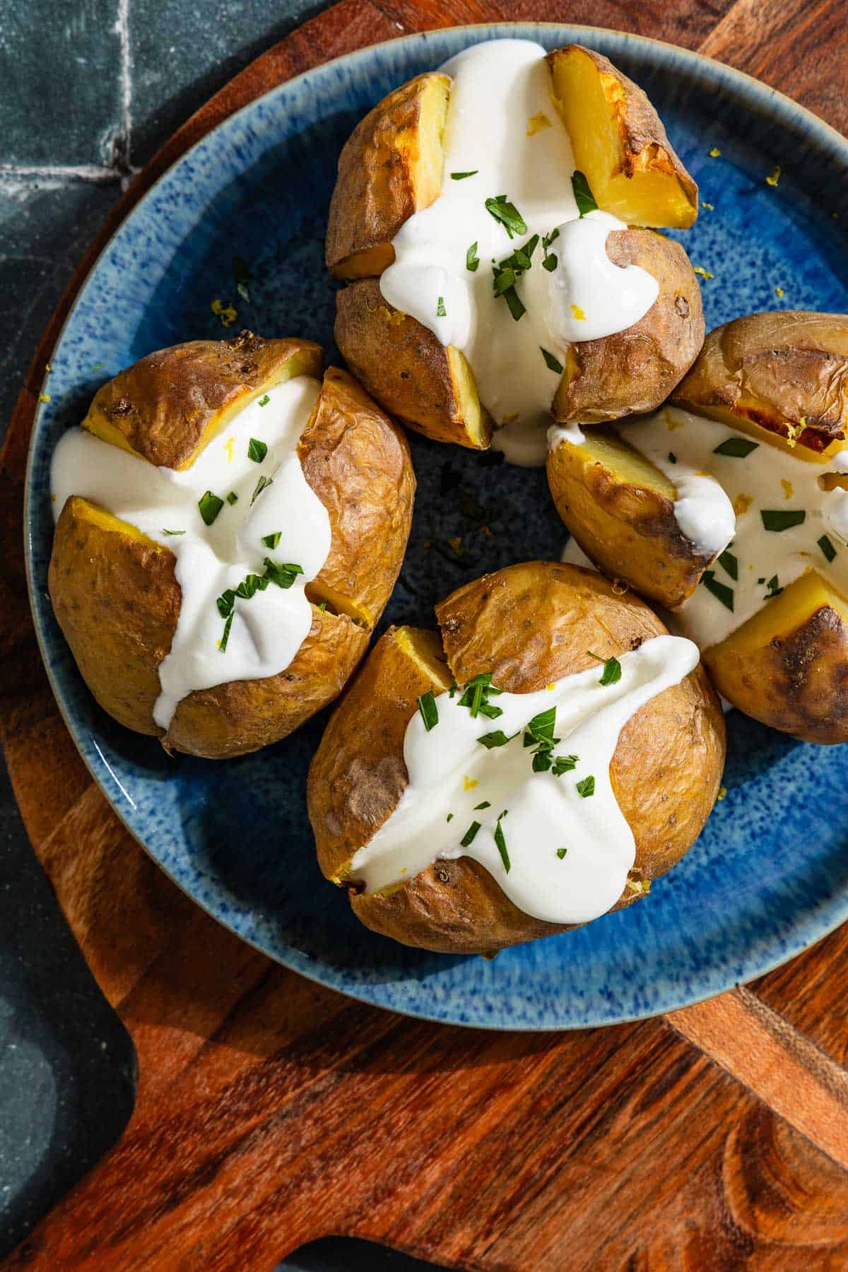 An overhead close up photo of 4 stuffed potatoes with feta on a serving platter sitting on a wooden cutting board.