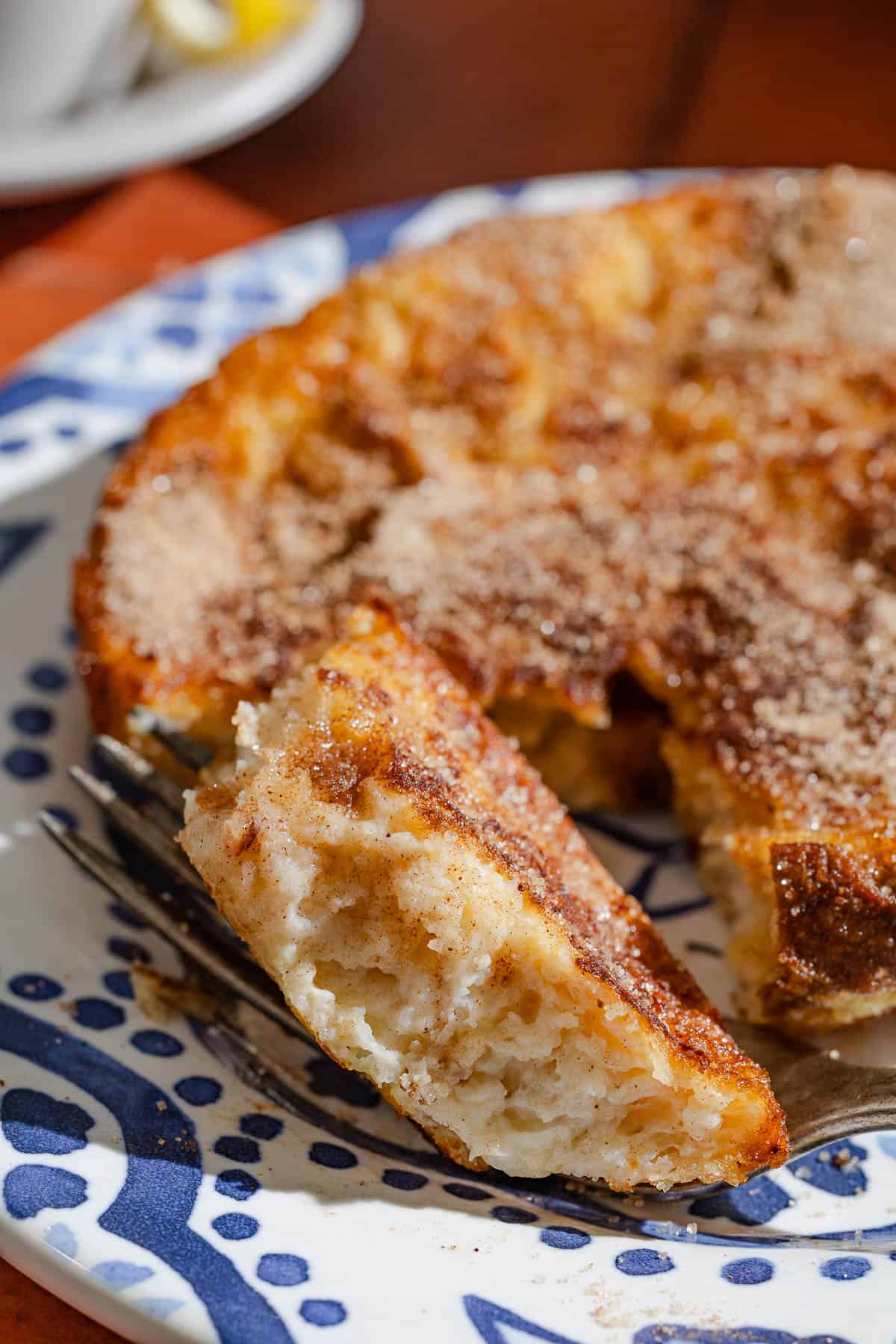 A close up of a torrija on a plate with a bite of it sitting on a fork.