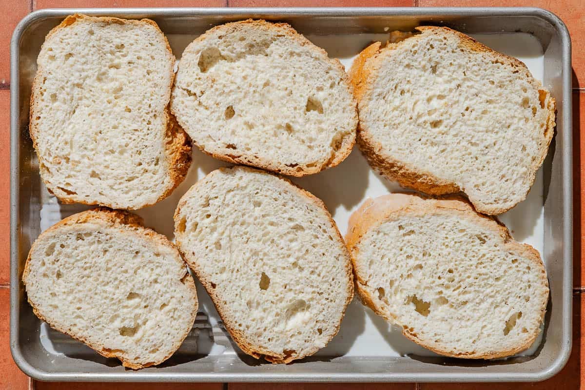 Six slices of bread on a baking sheet soaking in milk.