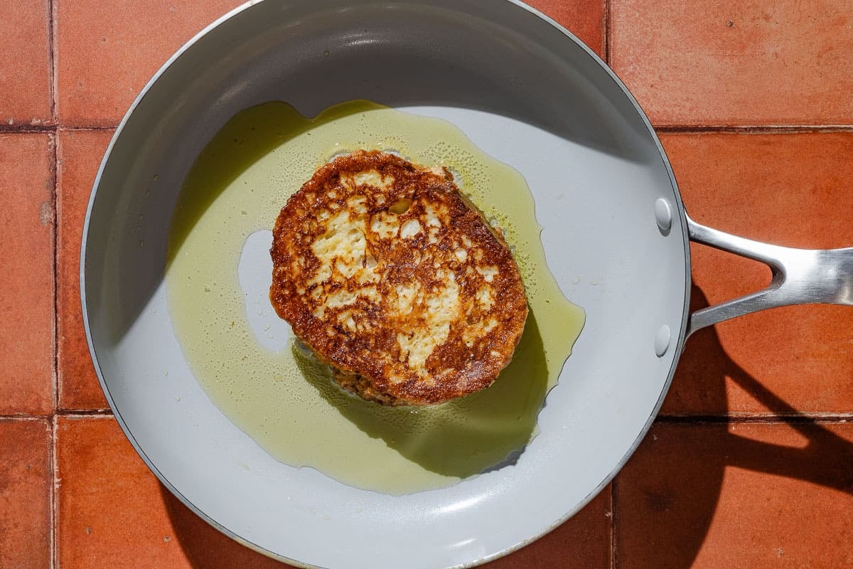 A torrija being fried in oil in a skillet.