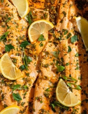 A close up of baked trout garnished with parsley, green onions and lemon wedges.