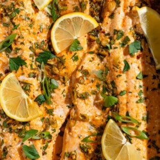 A close up of baked trout garnished with parsley, green onions and lemon wedges.