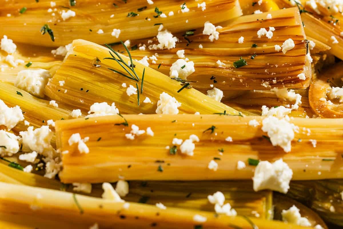 A close up photo of braised leeks garnished with dill and crumbled feta.