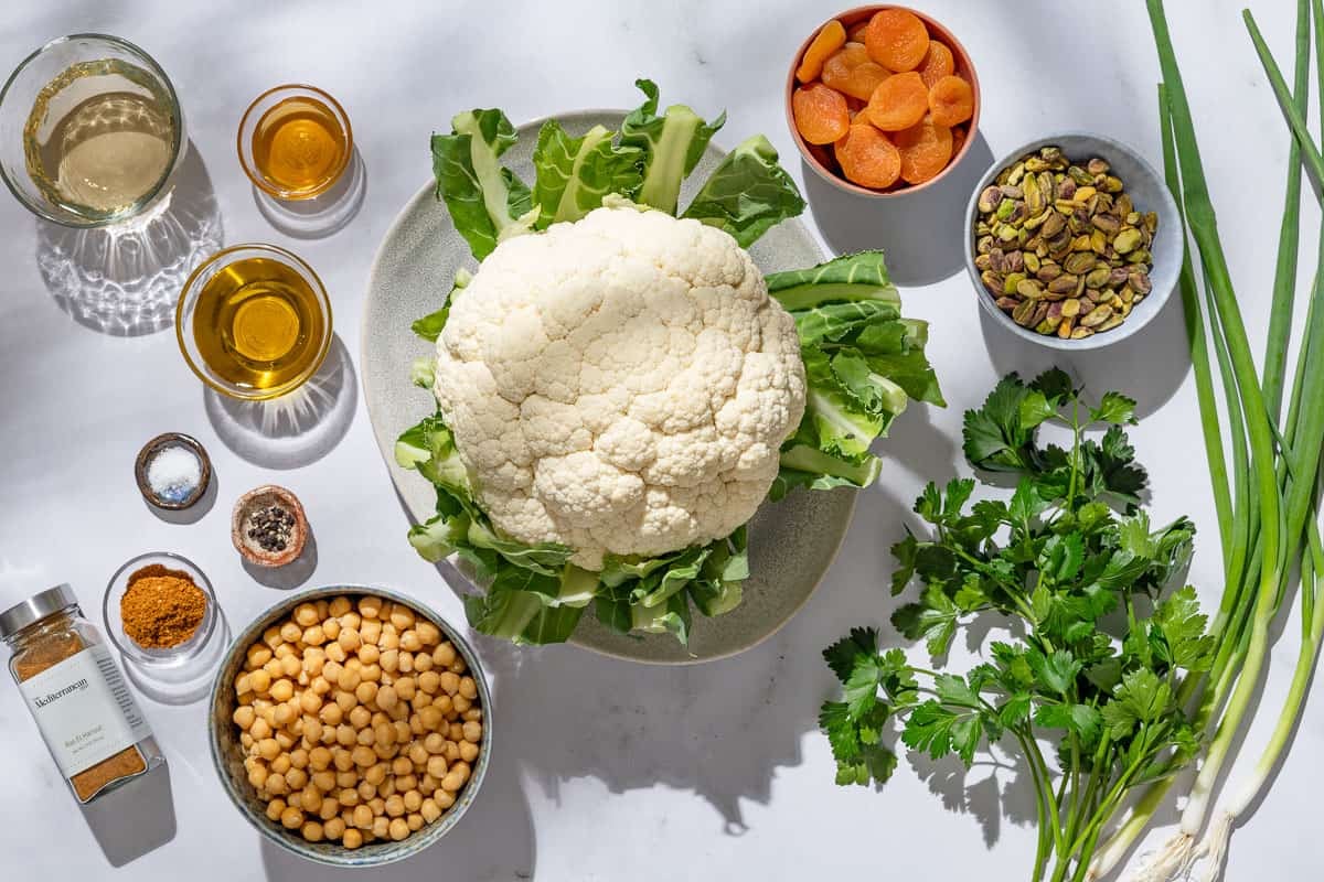 Ingredients for shaved cauliflower salad including cauliflower, pistachios, vinegar, honey, olive oil, ras el hanout, salt, pepper, chickpeas, scallions, dried apricots, and parsley.