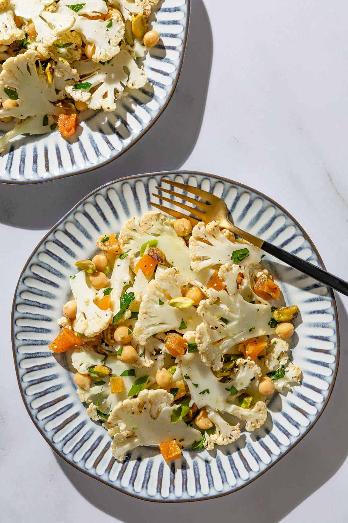 A close up of a shaved cauliflower salad on a plate with a fork with another in the background.